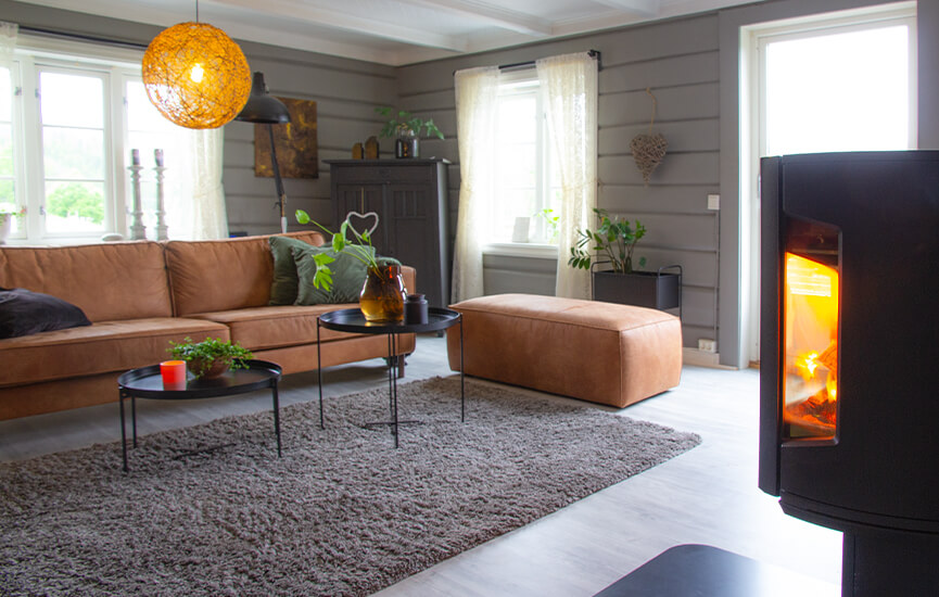 Braskamin i grått vardagsrum med timmerväggar och brun soffa