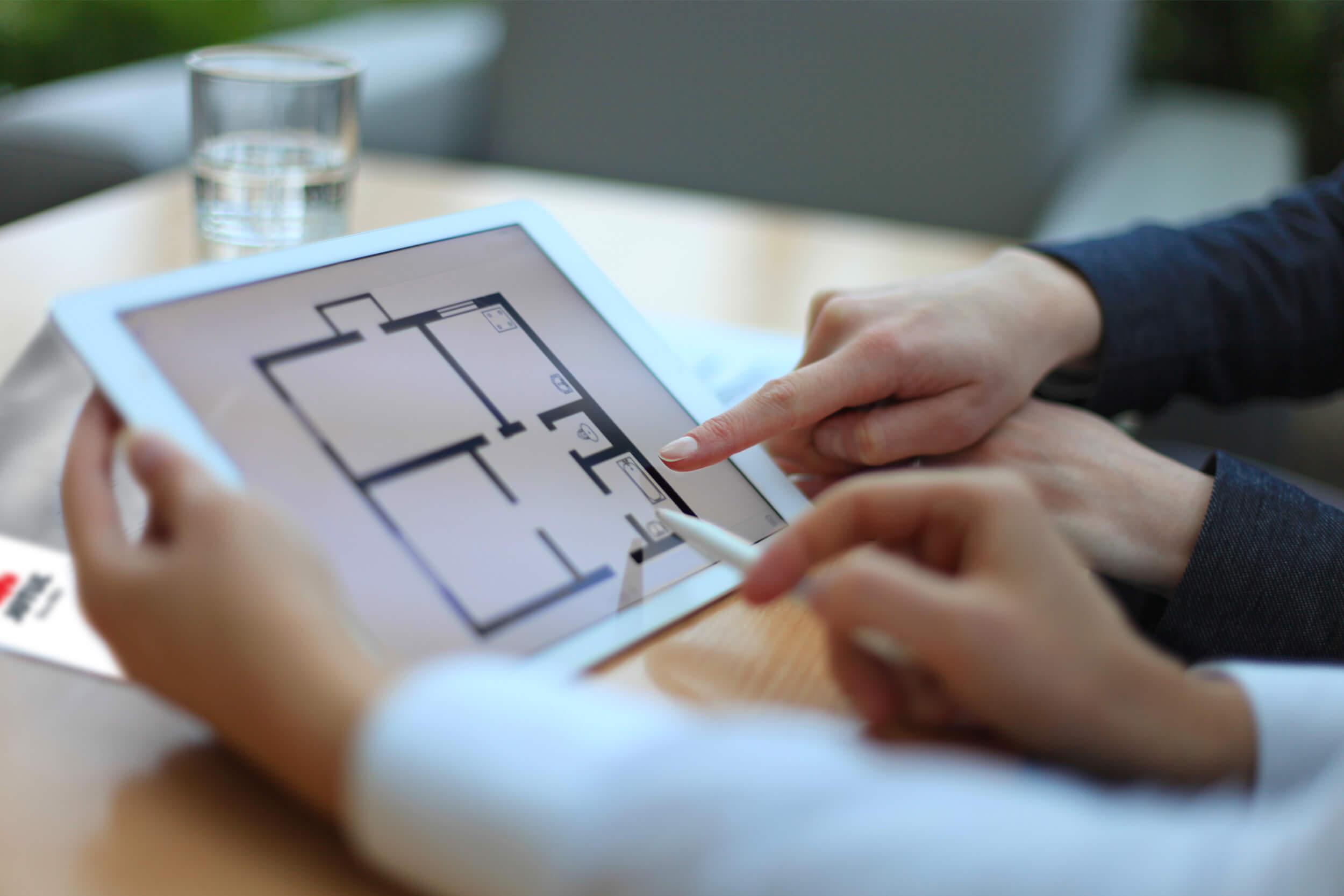 Händer som pekar på iPad med ark med rumsfördelning i ett hus.