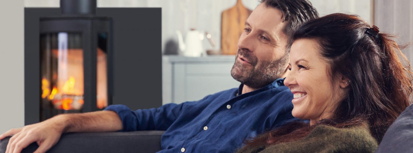 Man och kvinna sitter framför braskaminen Jøtul F 373 Advance i vardagsrummet